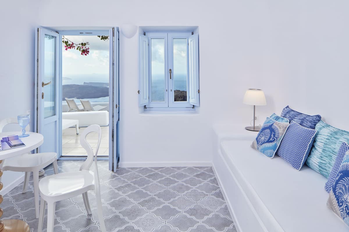 A room with a white sofa, a dining table with chairs, a window with a view, and a lamp.