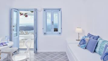 A room with a white sofa, a dining table with chairs, a window with a view, and a lamp.