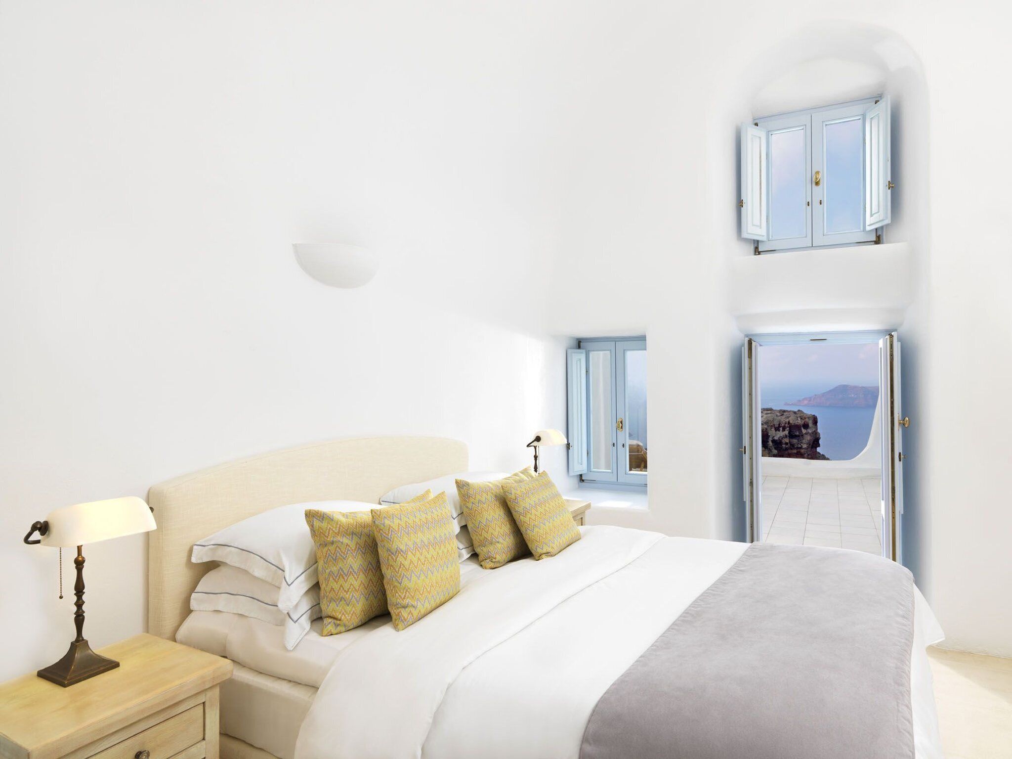 A bedroom with a bed, nightstand, lamp, and two windows with blue shutters.