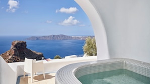 A white-walled room with a view of the sea and a tiled bathtub. - Astra Suites (Santorini)