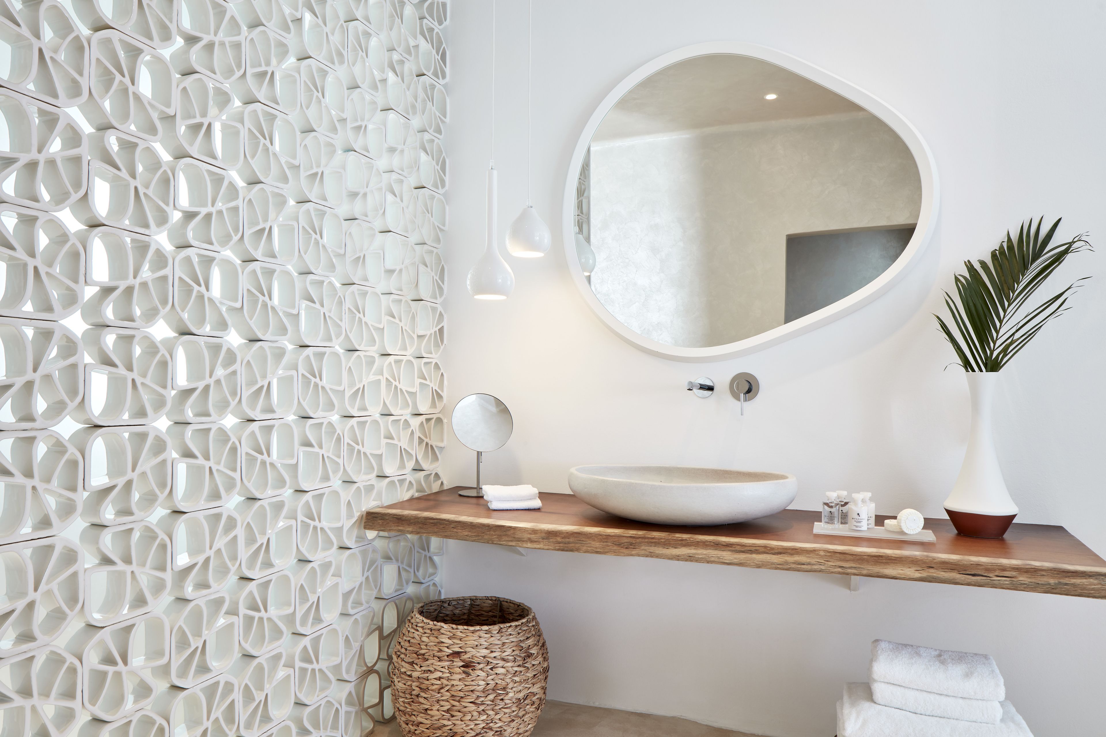 A modern bathroom with a geometric wall design, a round mirror, a wooden vanity, and a large vessel sink.