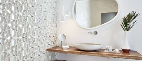 A modern bathroom with a geometric wall design, a round mirror, a wooden vanity, and a large vessel sink.