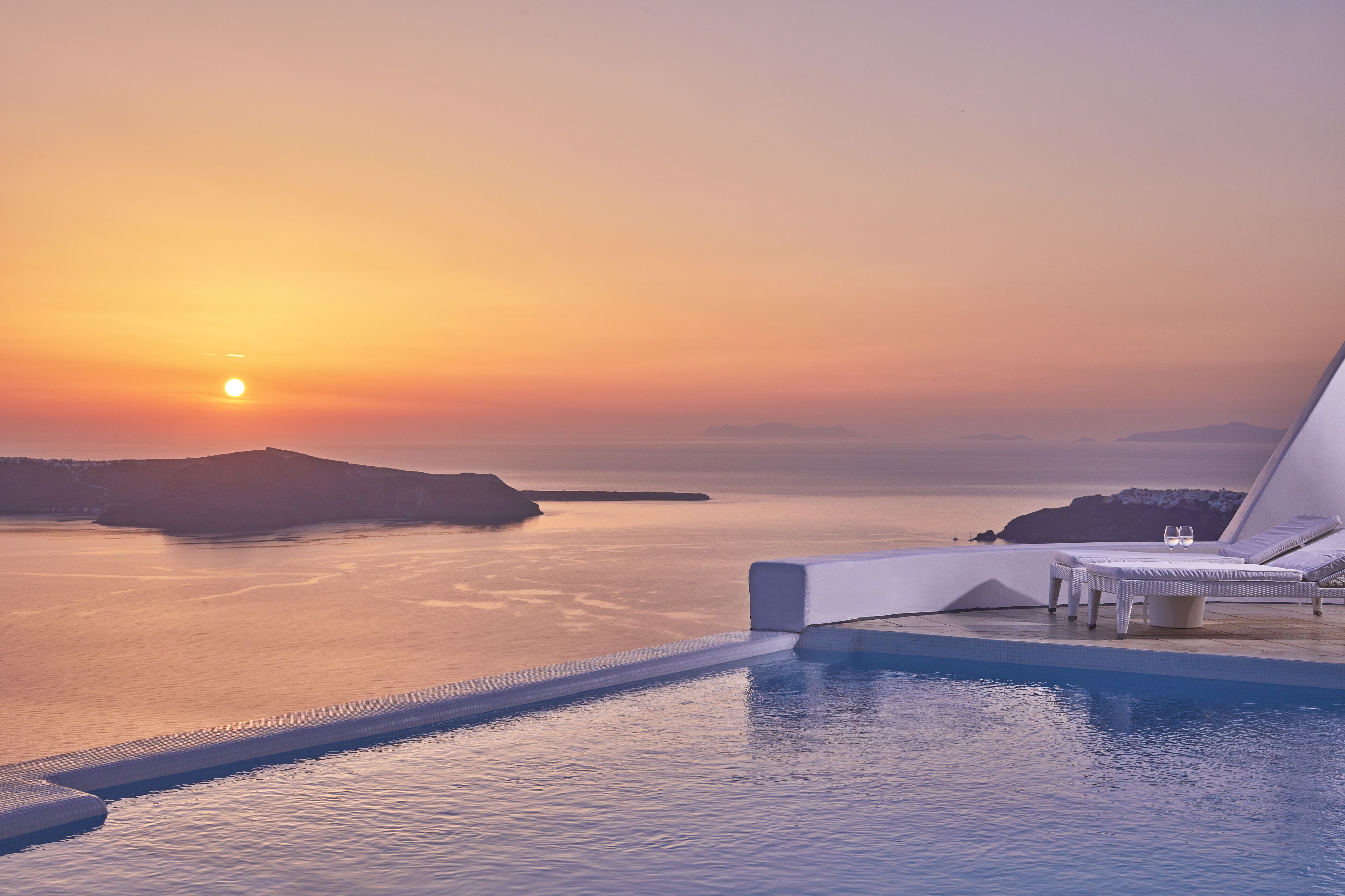 A sunset view from a poolside area with lounge chairs and a table.