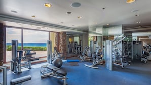 A gym with various exercise equipment, large windows with a view of the ocean, and a stone pillar. - Kumulani at Mauna Kea (Kamuela)