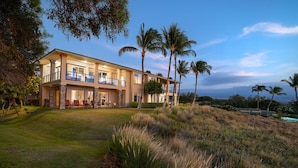 A two-story house with a balcony, surrounded by a well-maintained lawn and palm trees. - Kumulani at Mauna Kea (Kamuela)