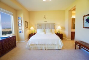 A bedroom with a large bed, two bedside tables with lamps, a dresser, and a window with a view.