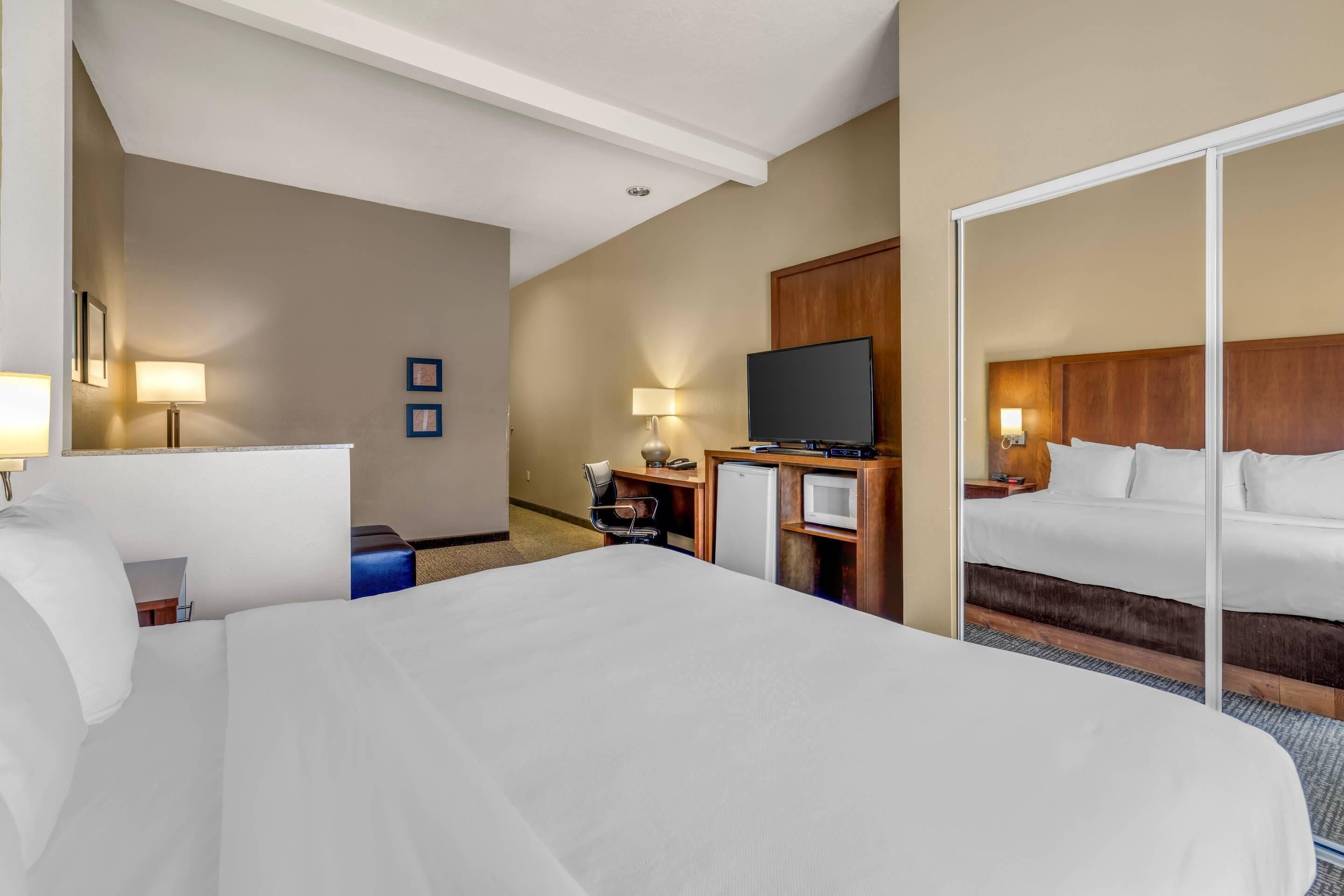 A hotel room with a large bed, a television, a desk with a computer, and a wardrobe.