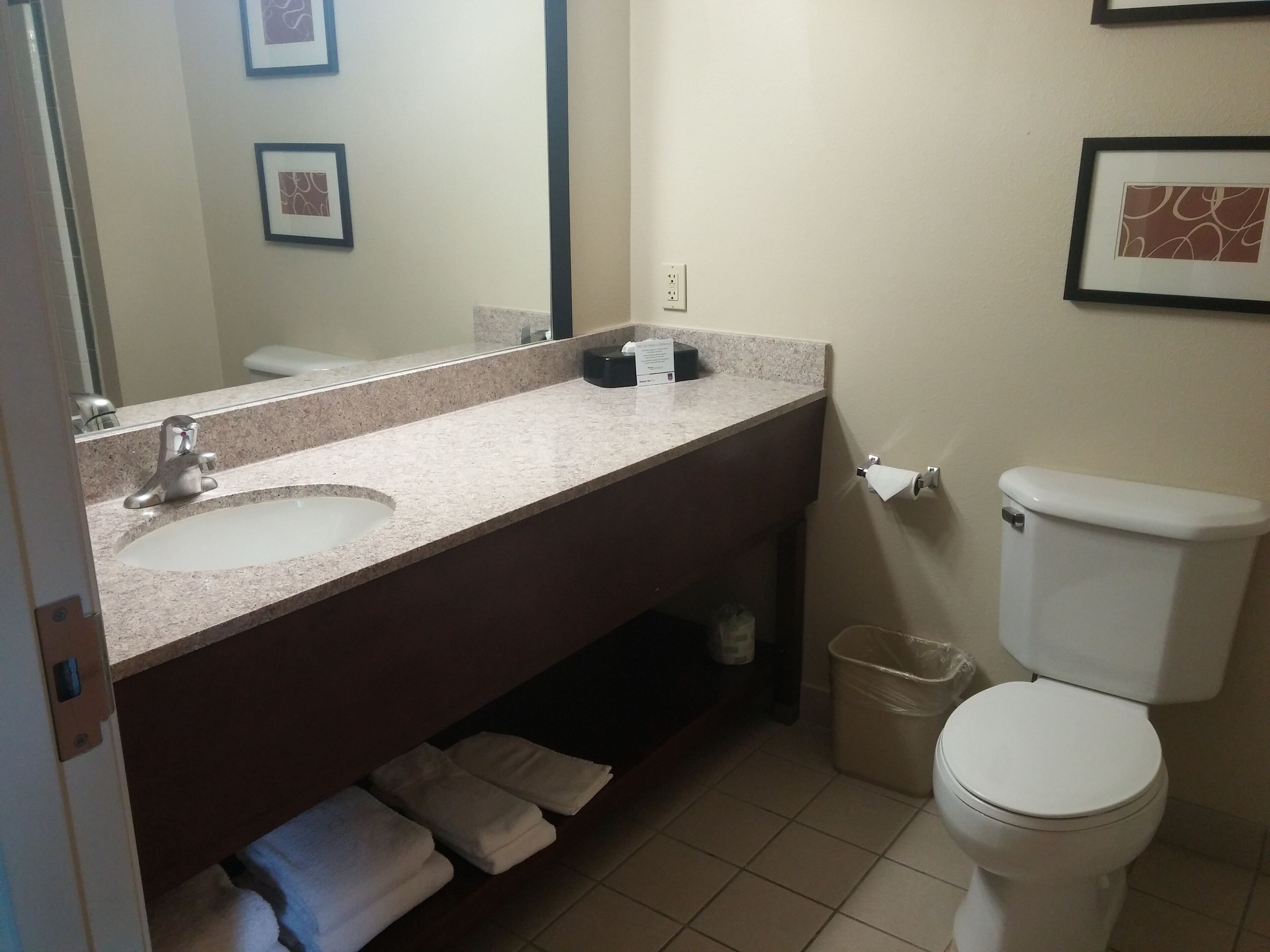 A bathroom with a sink, mirror, toilet, and a trash bin.