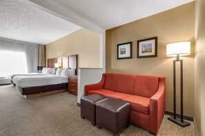 A hotel room with a bed, a sofa, an ottoman, a desk, and a lamp.
