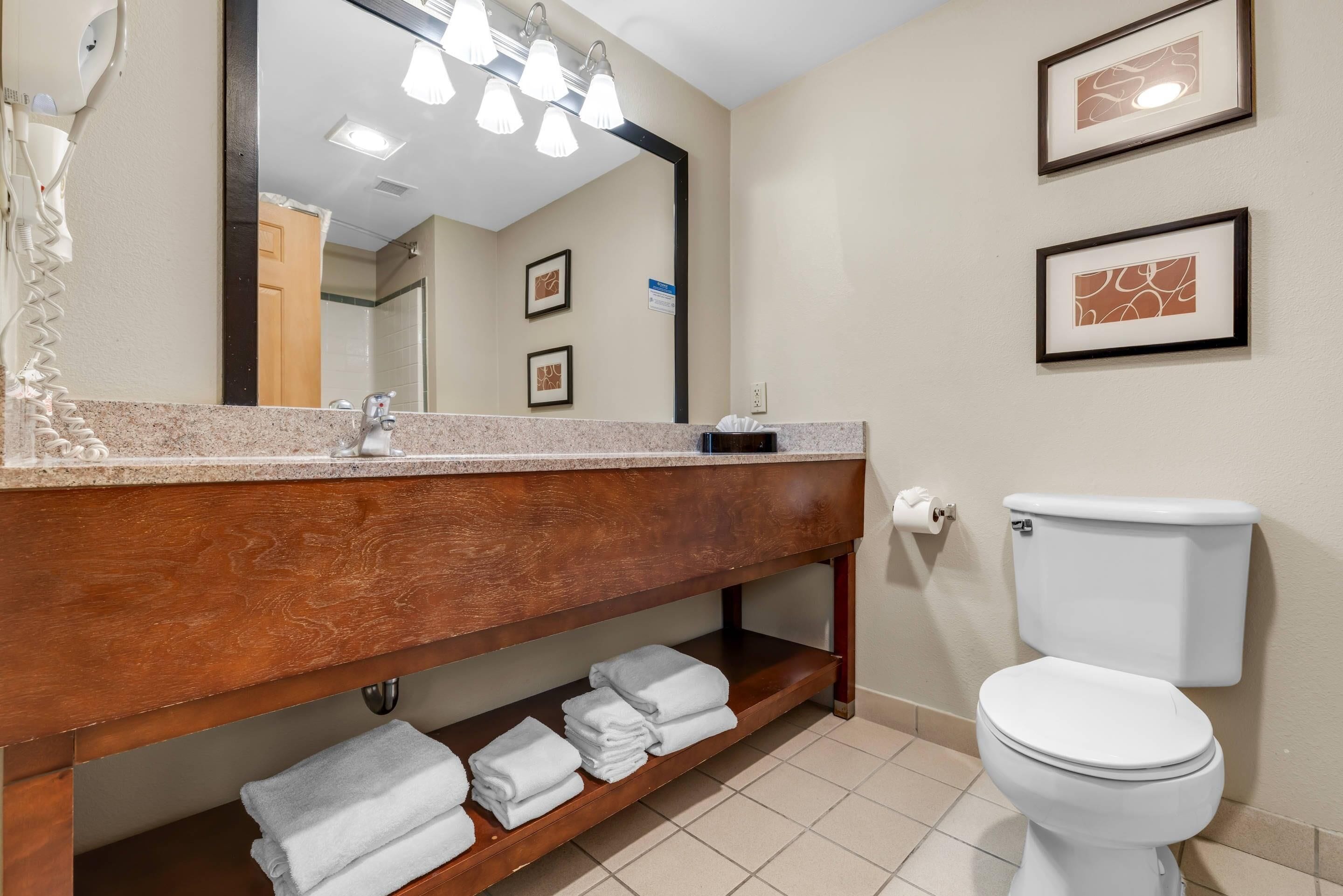 A bathroom with a wooden vanity, a sink, a toilet, and a mirror with lights.