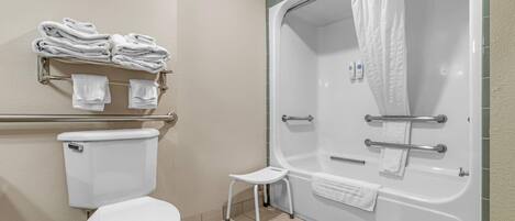 A bathroom with a toilet, a shower with a glass door, a small stool, and a towel rack with folded towels.