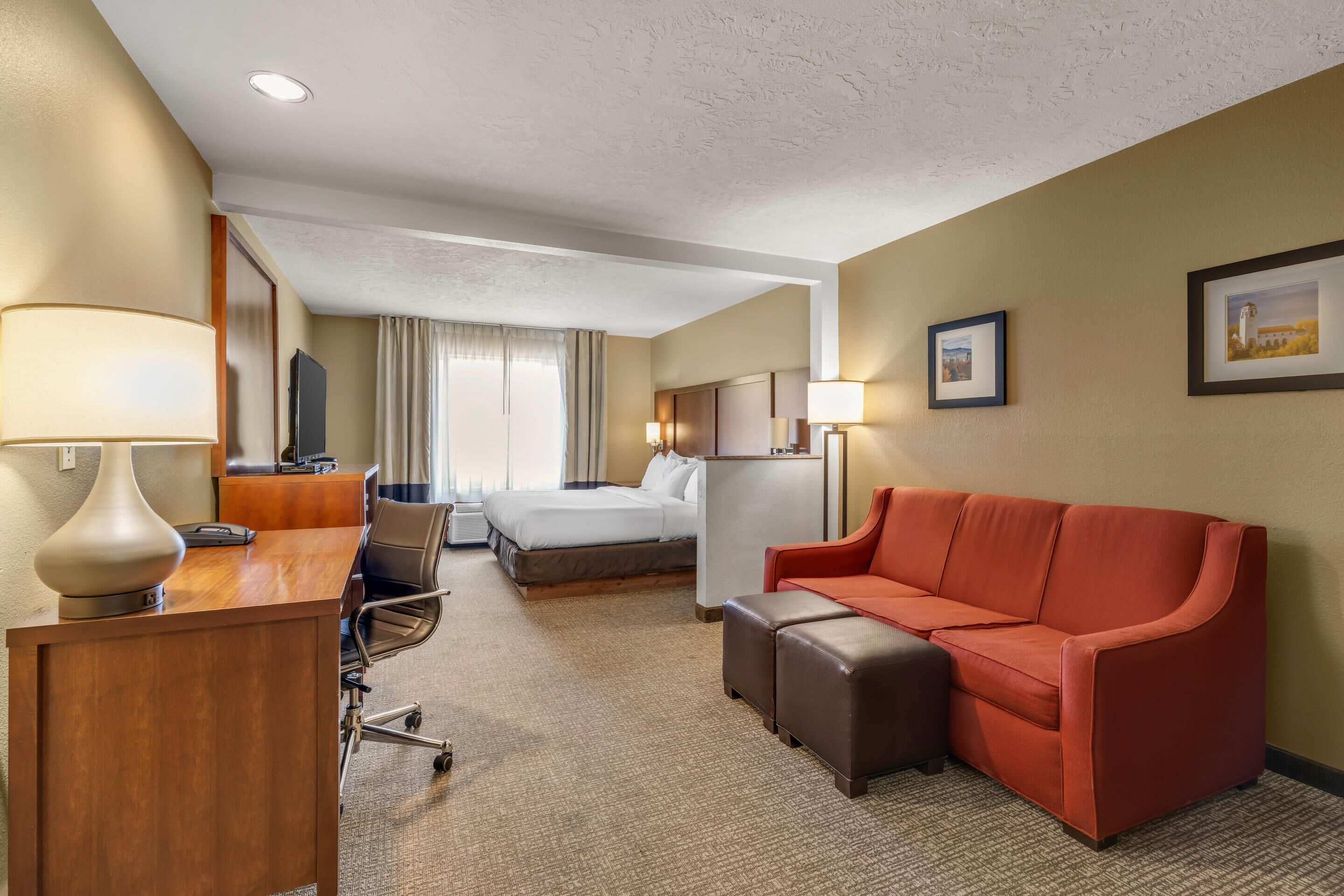 Een hotelkamer met een bed, een bureau met lamp, een rode bank en een kleine tafel.