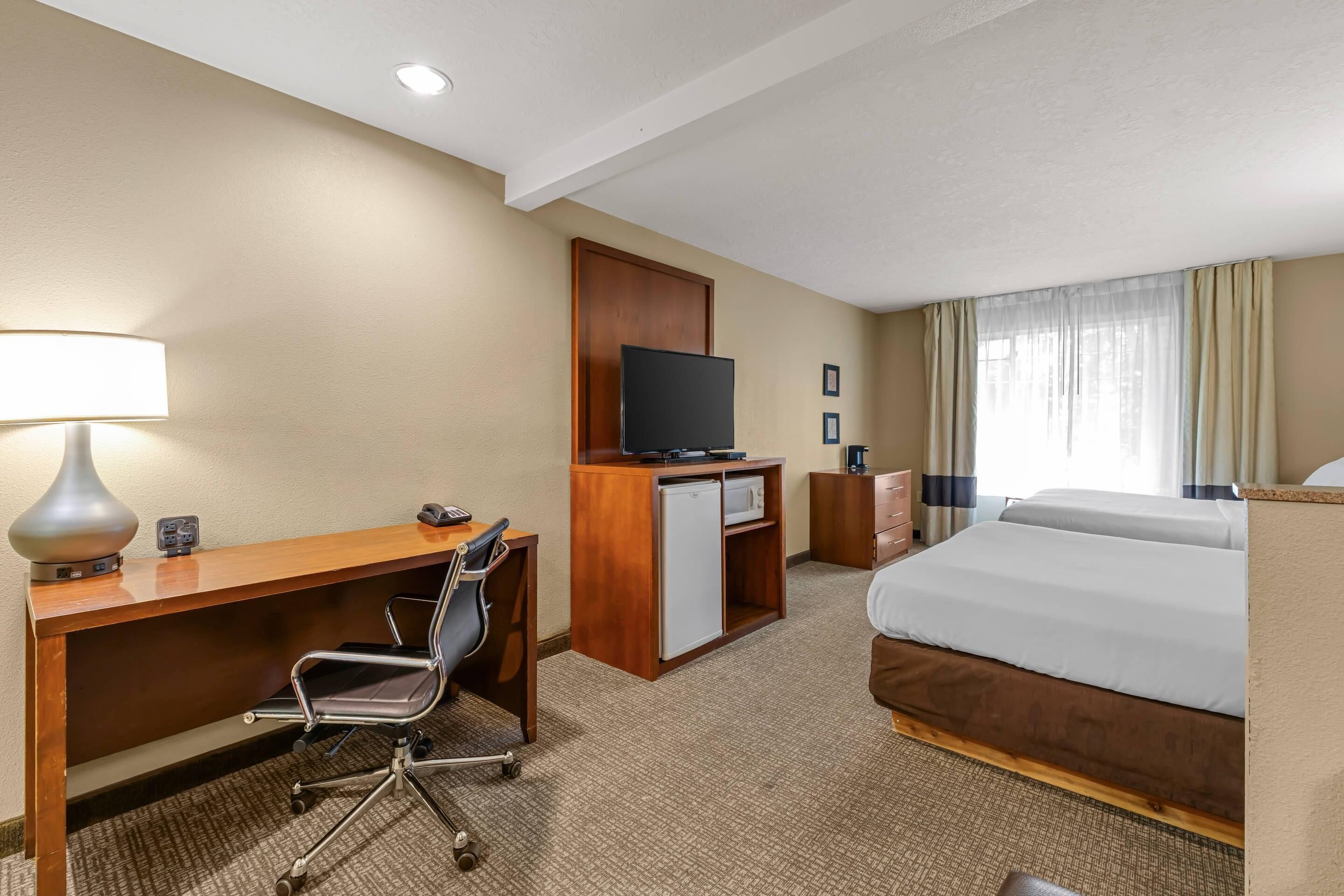 A hotel room with a desk, chair, television, minibar, and a bed.