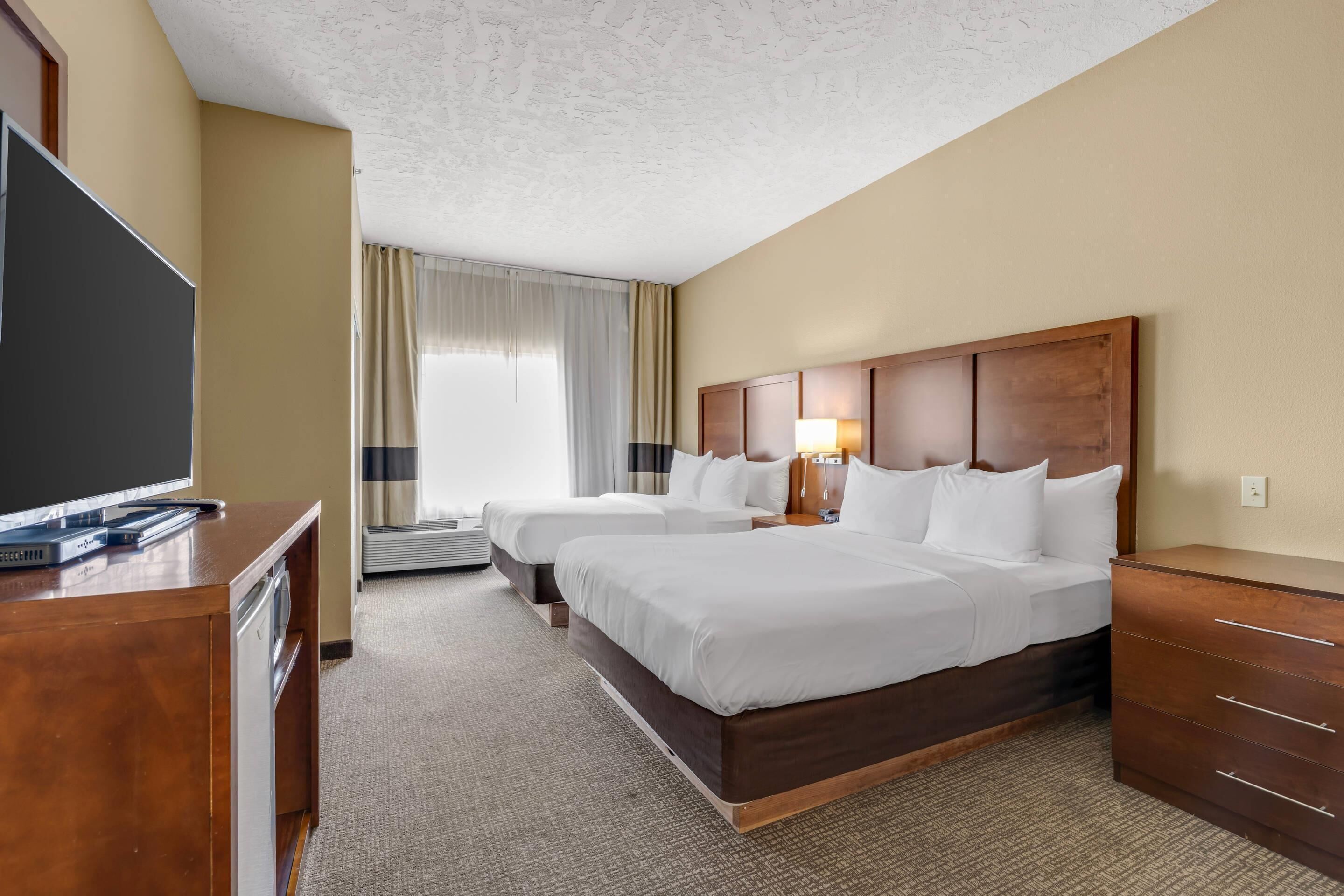 A hotel room with two beds, a TV, a desk, and a window with curtains.