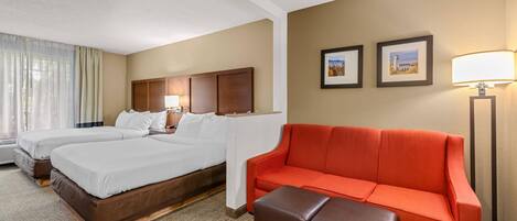 A hotel room with two beds, a red sofa, a brown ottoman, and a lamp.