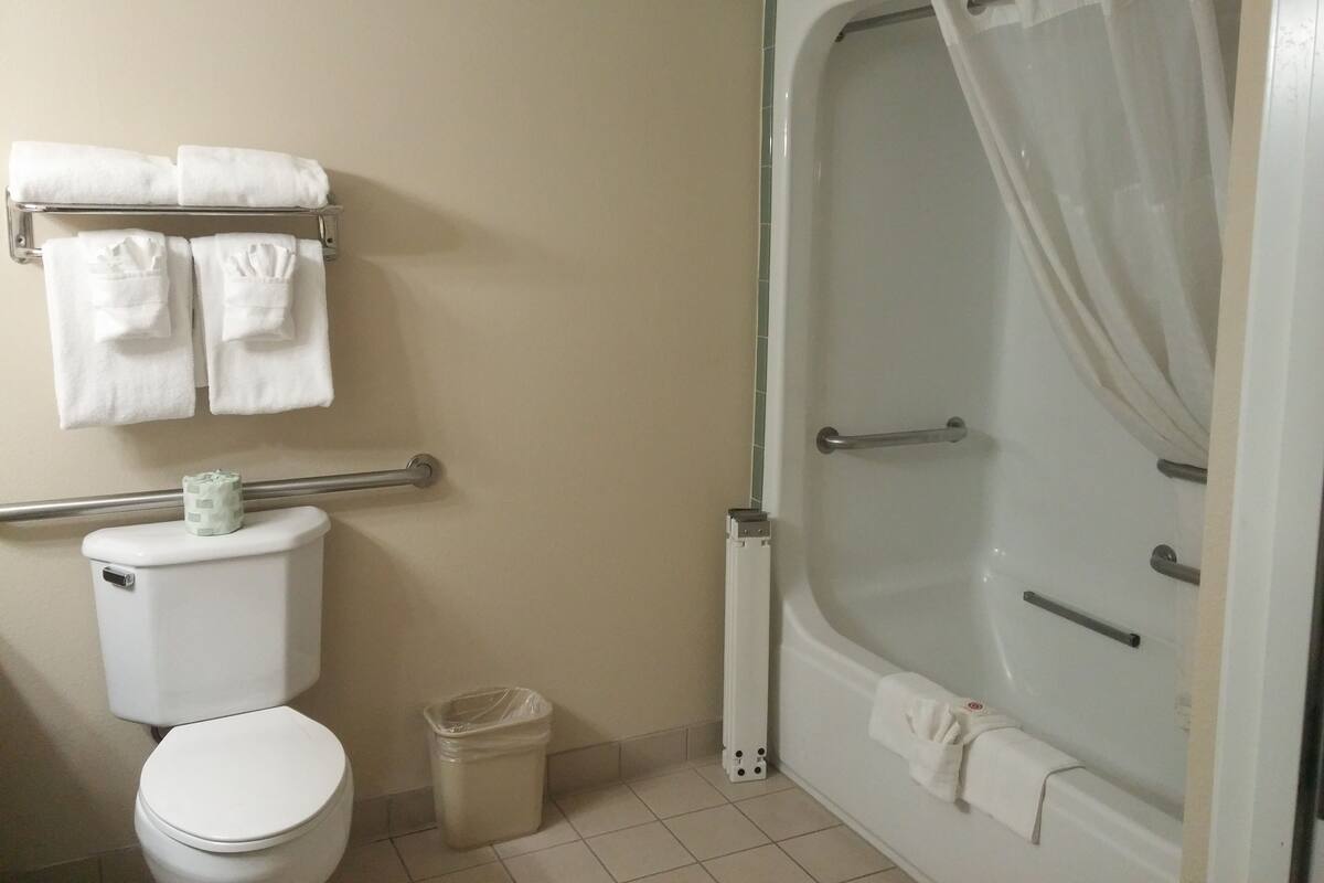 A bathroom with a toilet, a trash can, a towel rack with towels, and a bathtub with a shower curtain.