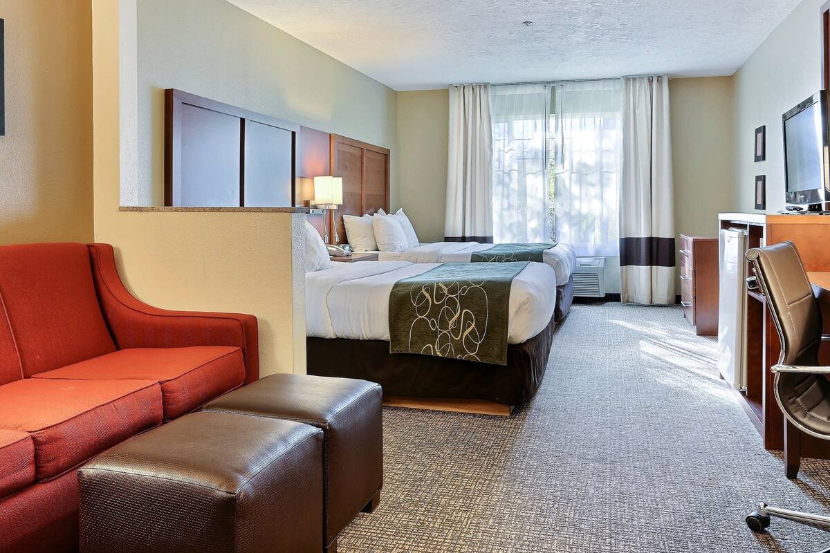 A hotel room with a bed, a desk, a red sofa, and a brown ottoman.