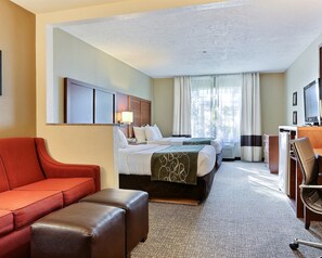 A hotel room with a bed, a desk, a red sofa, and a brown ottoman.