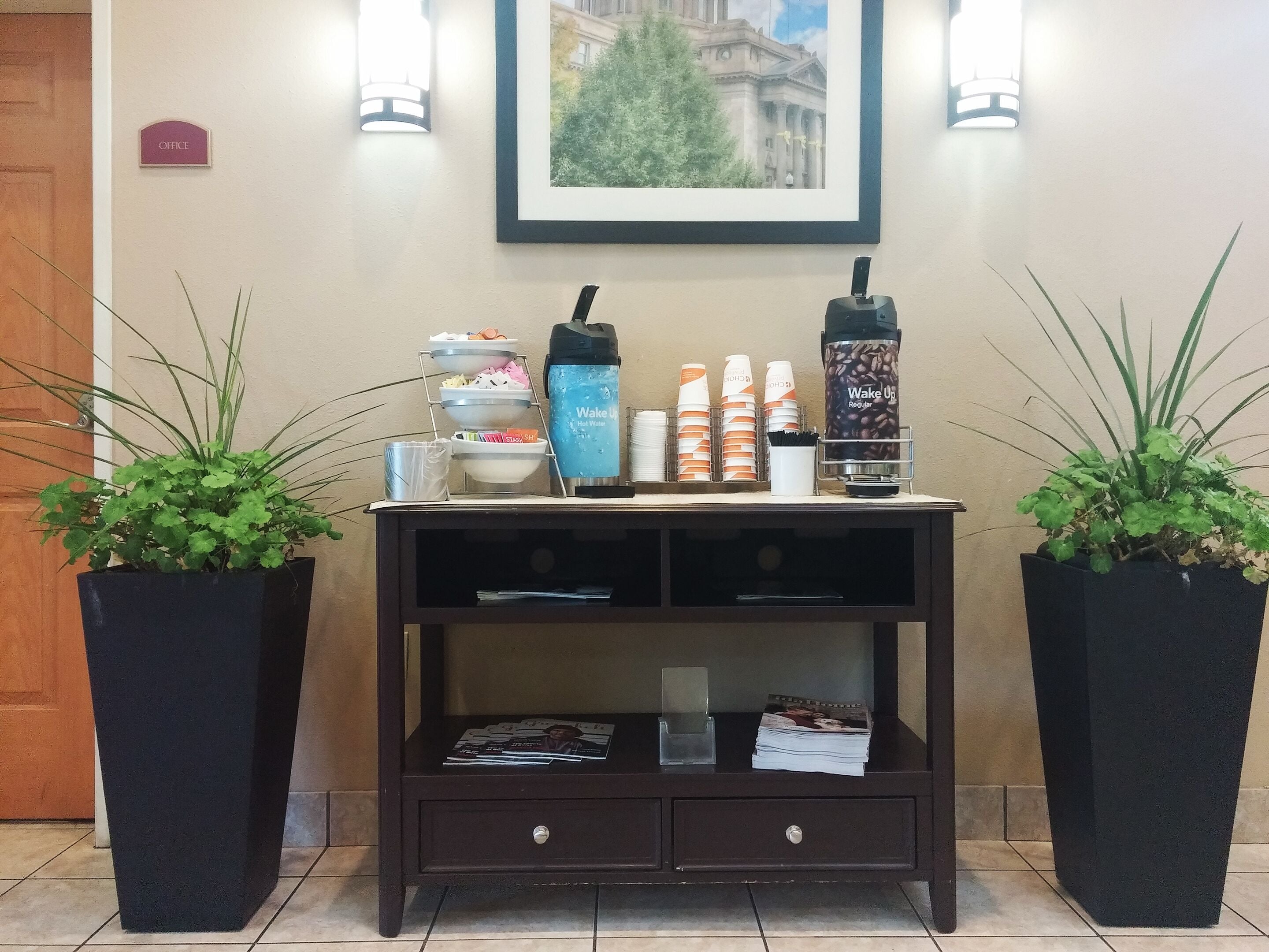 Taulell de recepció amb una zona de cafè, dues plantes en testos, un quadre amb marc i un senyal que indica l'oficina.