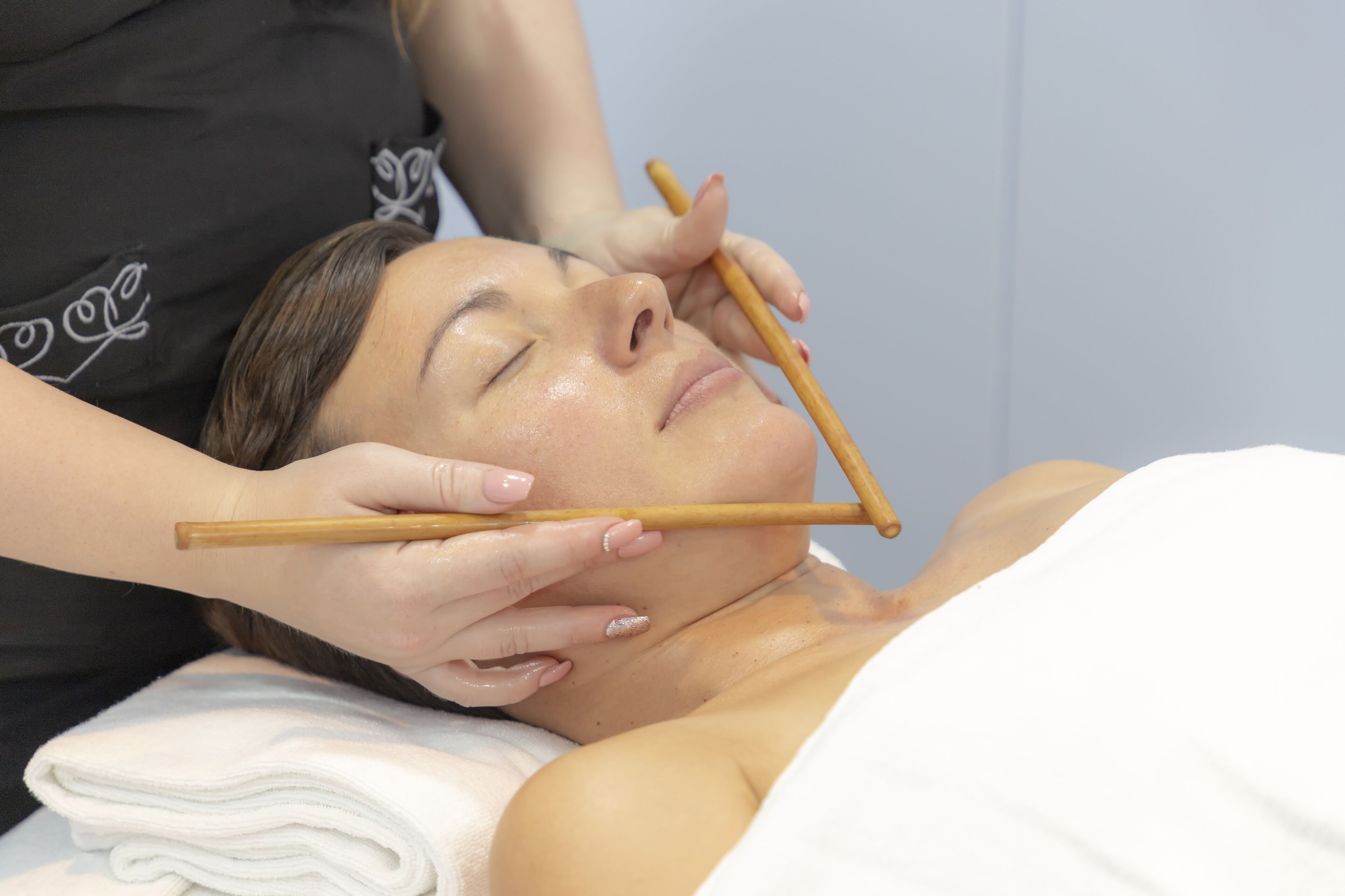 A person receiving a facial treatment with wooden tools.