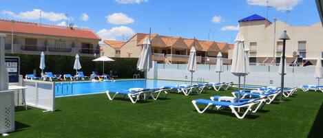A pool area with lounge chairs and umbrellas, surrounded by buildings with red-tiled roofs.