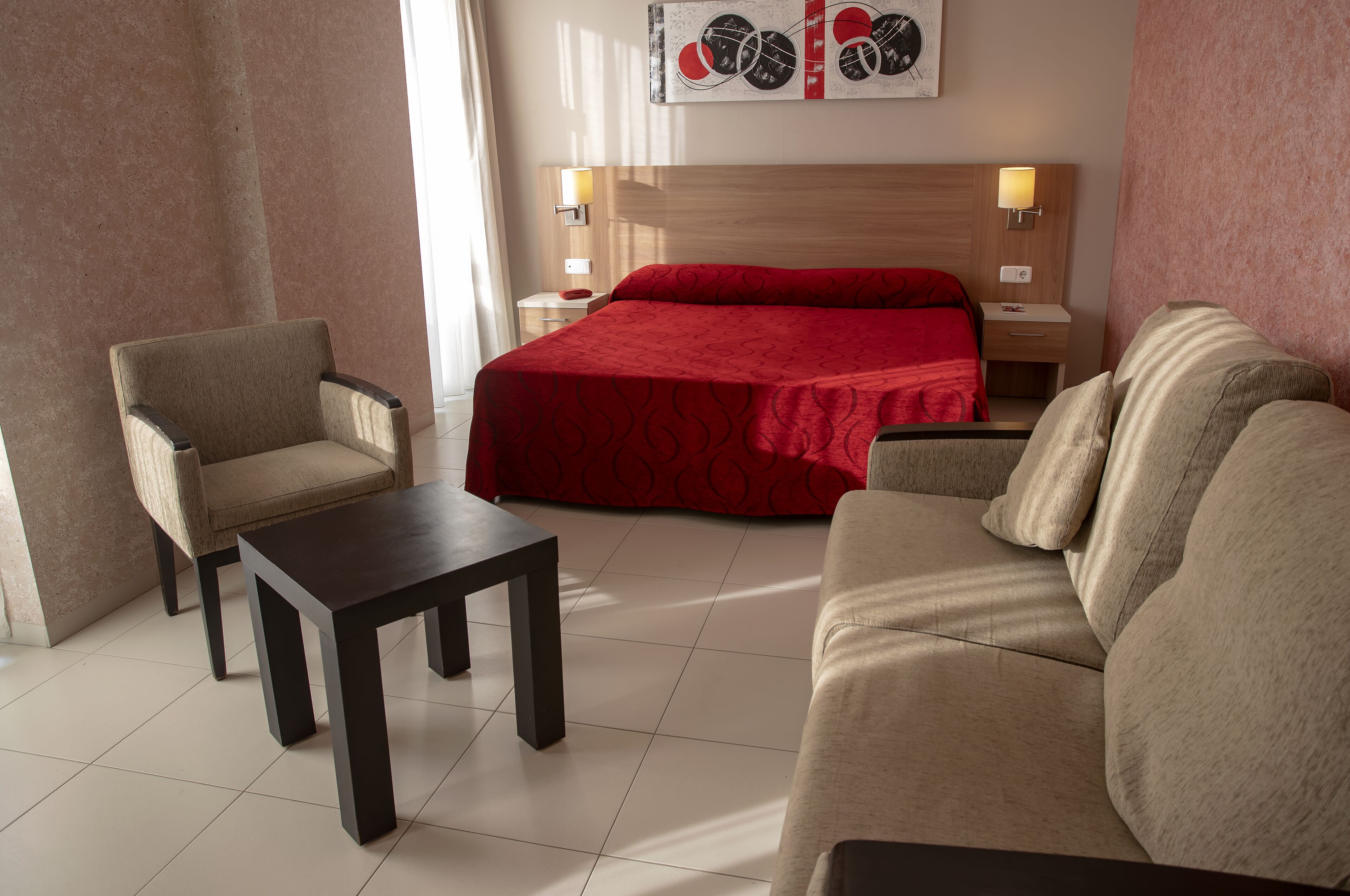A hotel room with a bed, two armchairs, a small table, and a nightstand with lamps.