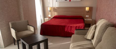 A hotel room with a bed, two armchairs, a small table, and a nightstand with lamps.