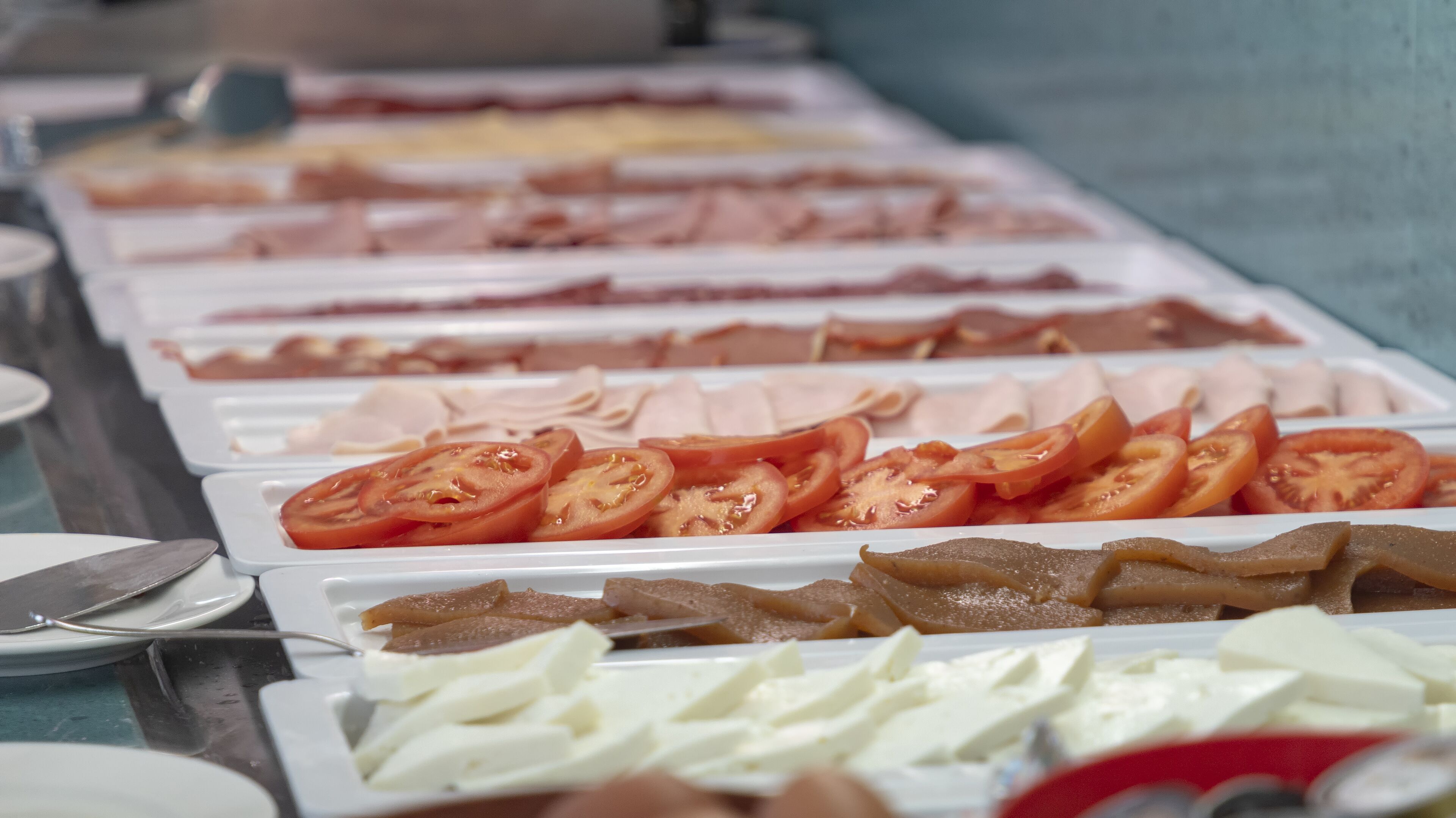 A buffet with various food items including sliced tomatoes, meats, and cheeses.