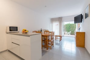 Una cocina moderna con microondas, mesa de comedor y sillas. Hay una pequeña isla con un frutero. La habitación tiene un ventanal con cortinas y vistas a zonas verdes.