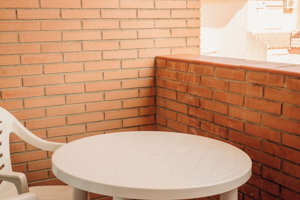 A corner of a room with a brick wall and a white table and chair.
