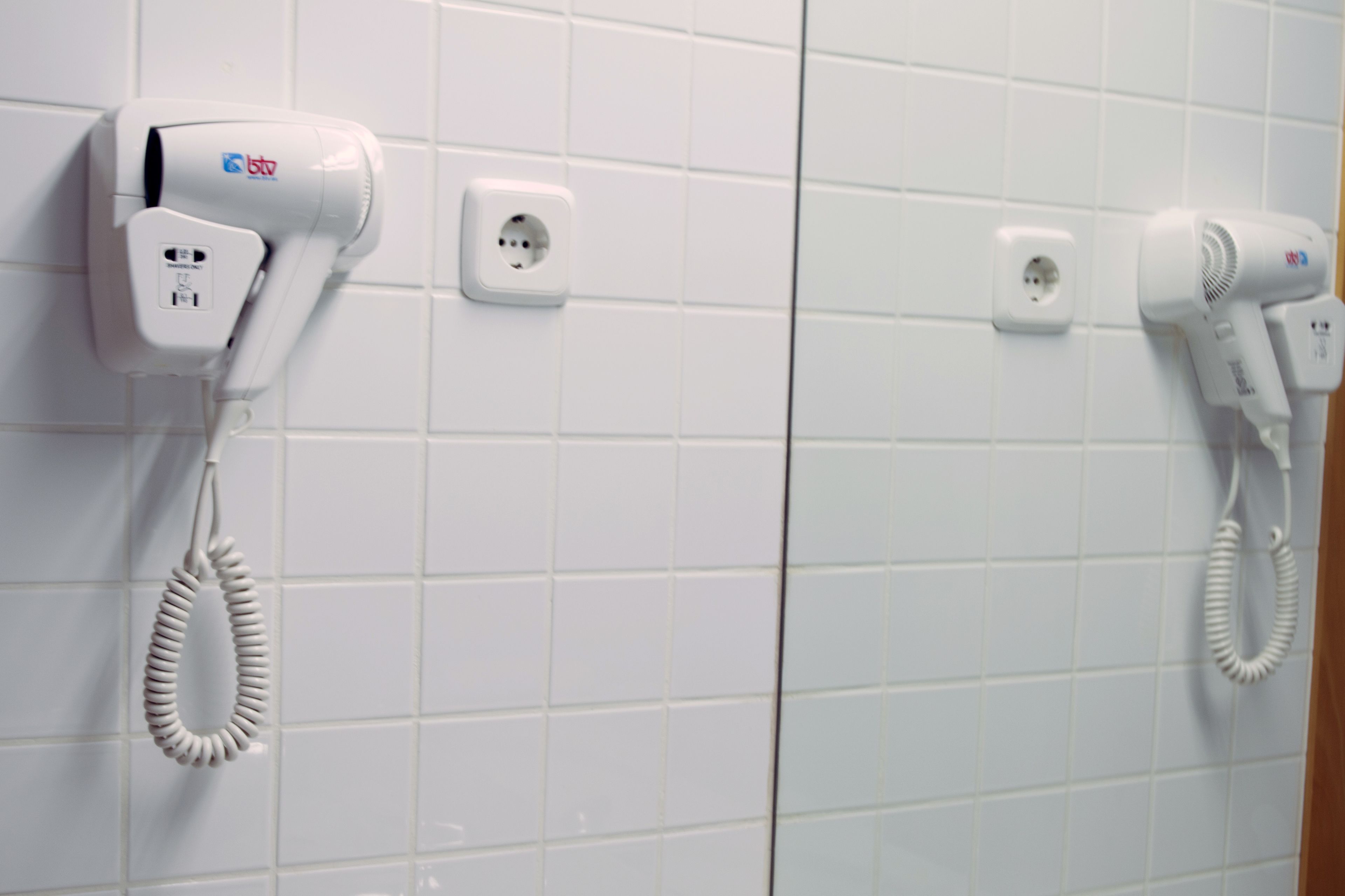 A bathroom with two hair dryers mounted on the wall, each with a power outlet.