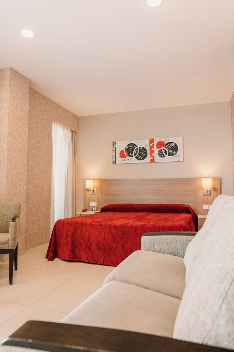 A hotel room with a bed, a sofa, a chair, and a wall-mounted artwork.