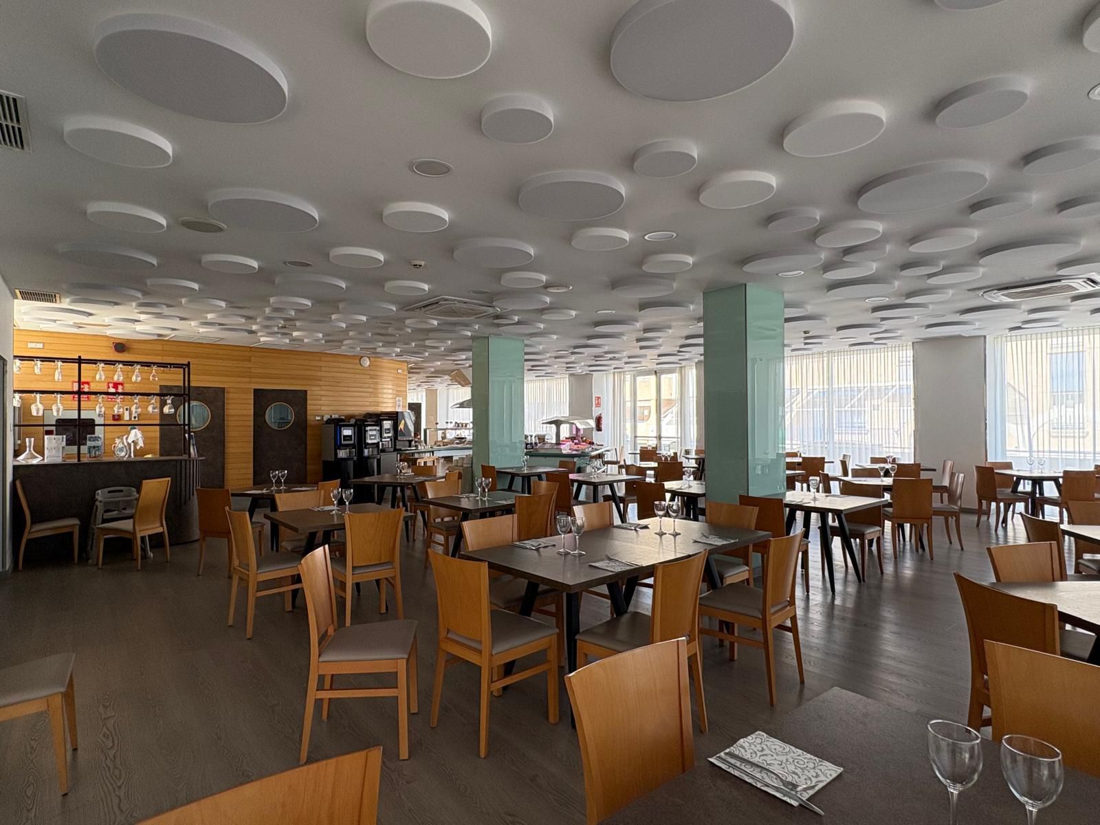 Een restaurantinterieur met ronde plafondlampen, houten tafels en stoelen.
