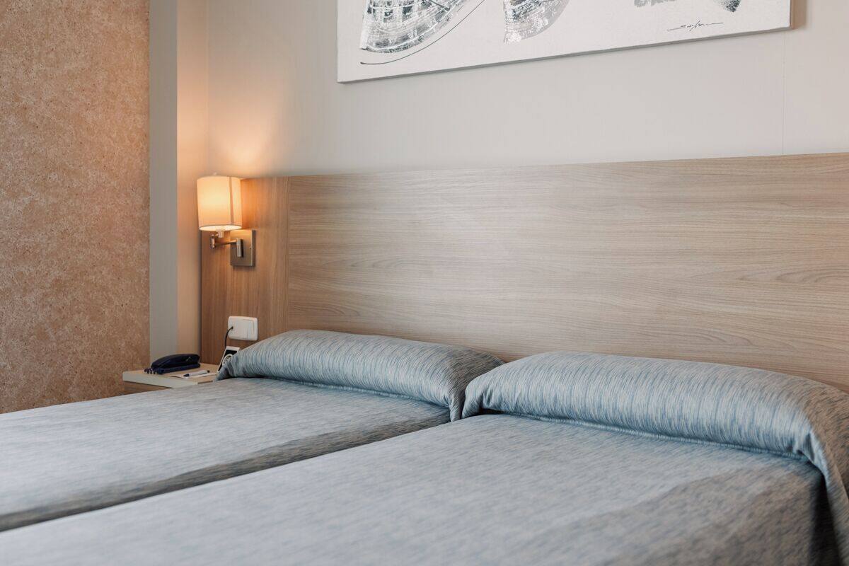 A hotel room with two beds, a nightstand with a lamp, and a wall-mounted artwork.