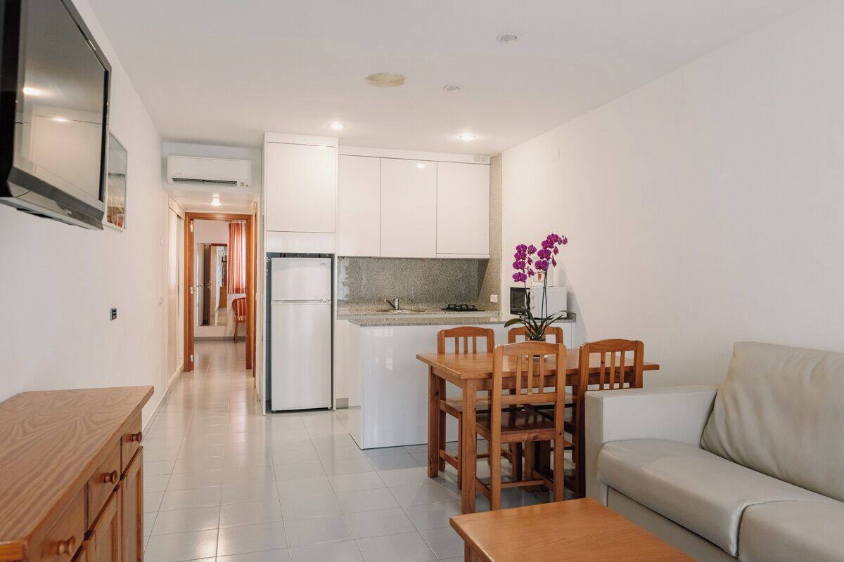 A modern kitchen with white cabinets, a dining table with chairs, and a sofa.