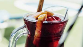 A glass pitcher with a straw and a cinnamon stick, containing a dark beverage with ice cubes.