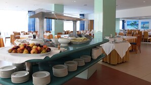 Zona de bufé con diversas frutas, recipientes y platos apilados.