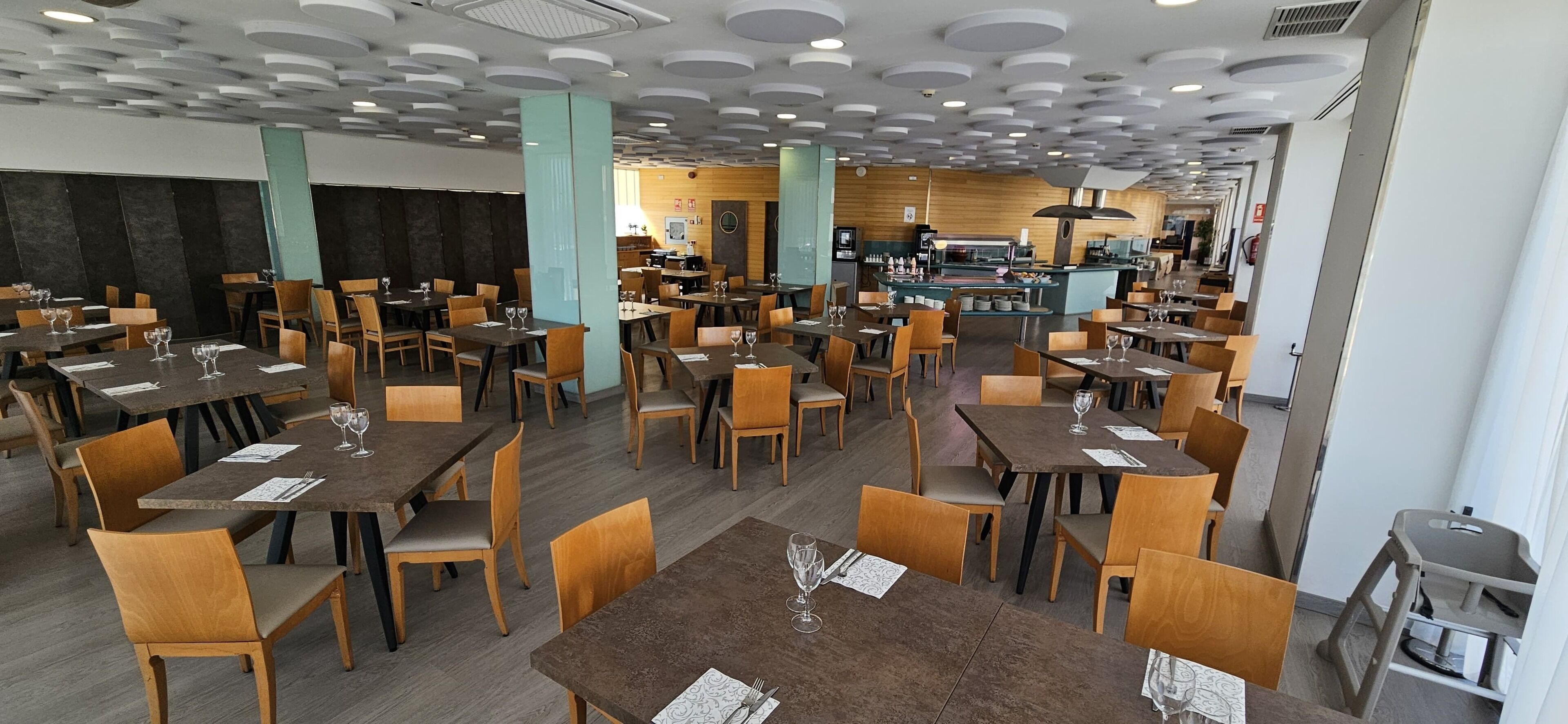A restaurant with multiple tables and chairs, a kitchen area, and a modern ceiling design.