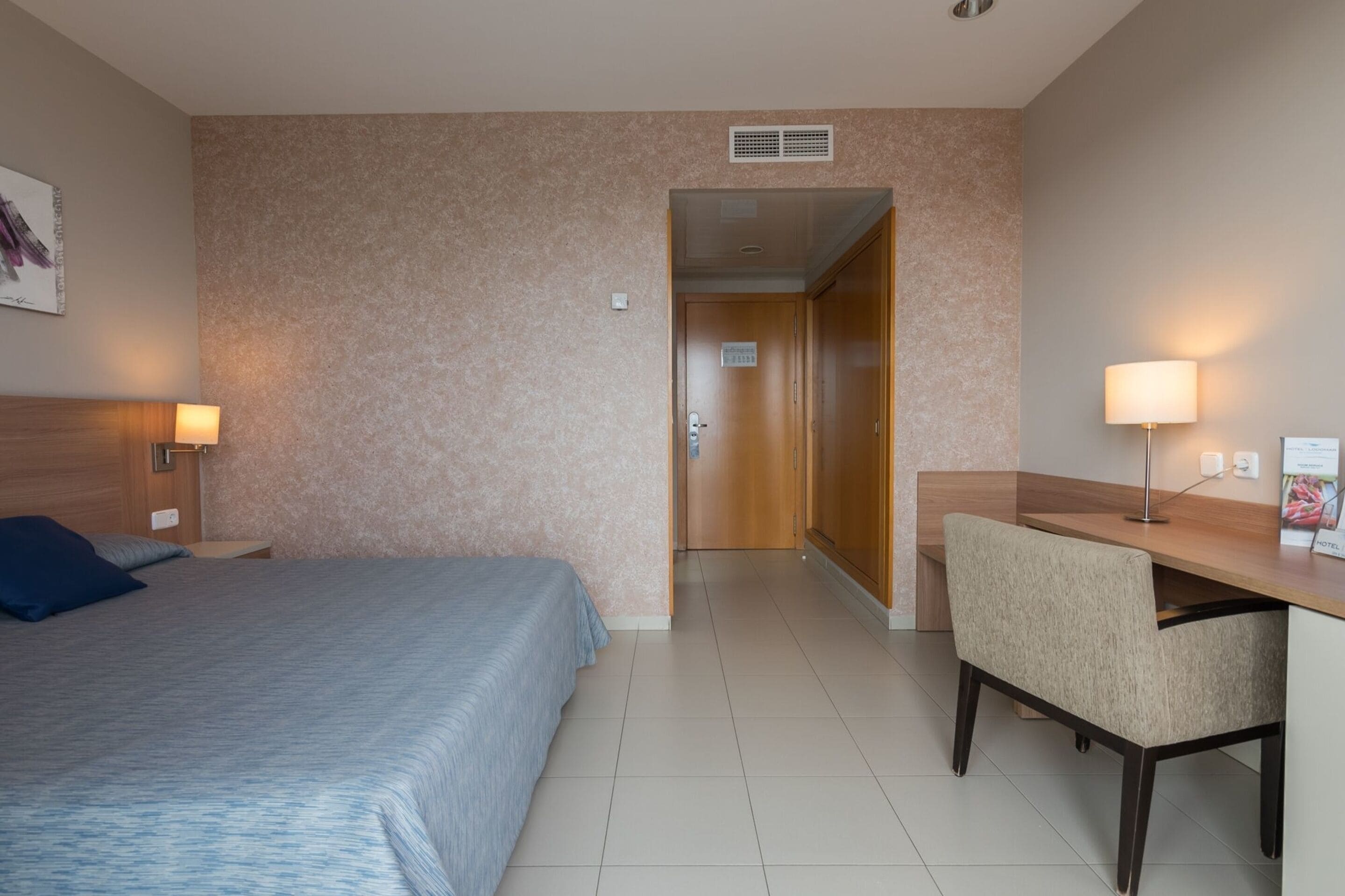 Habitación de hotel con cama, escritorio y silla. Se ve una puerta que da a otra habitación.