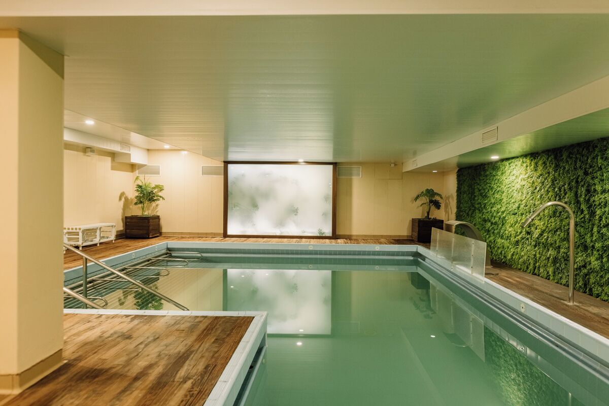 A modern indoor pool with clear water, wooden flooring, and a green wall with a textured pattern.