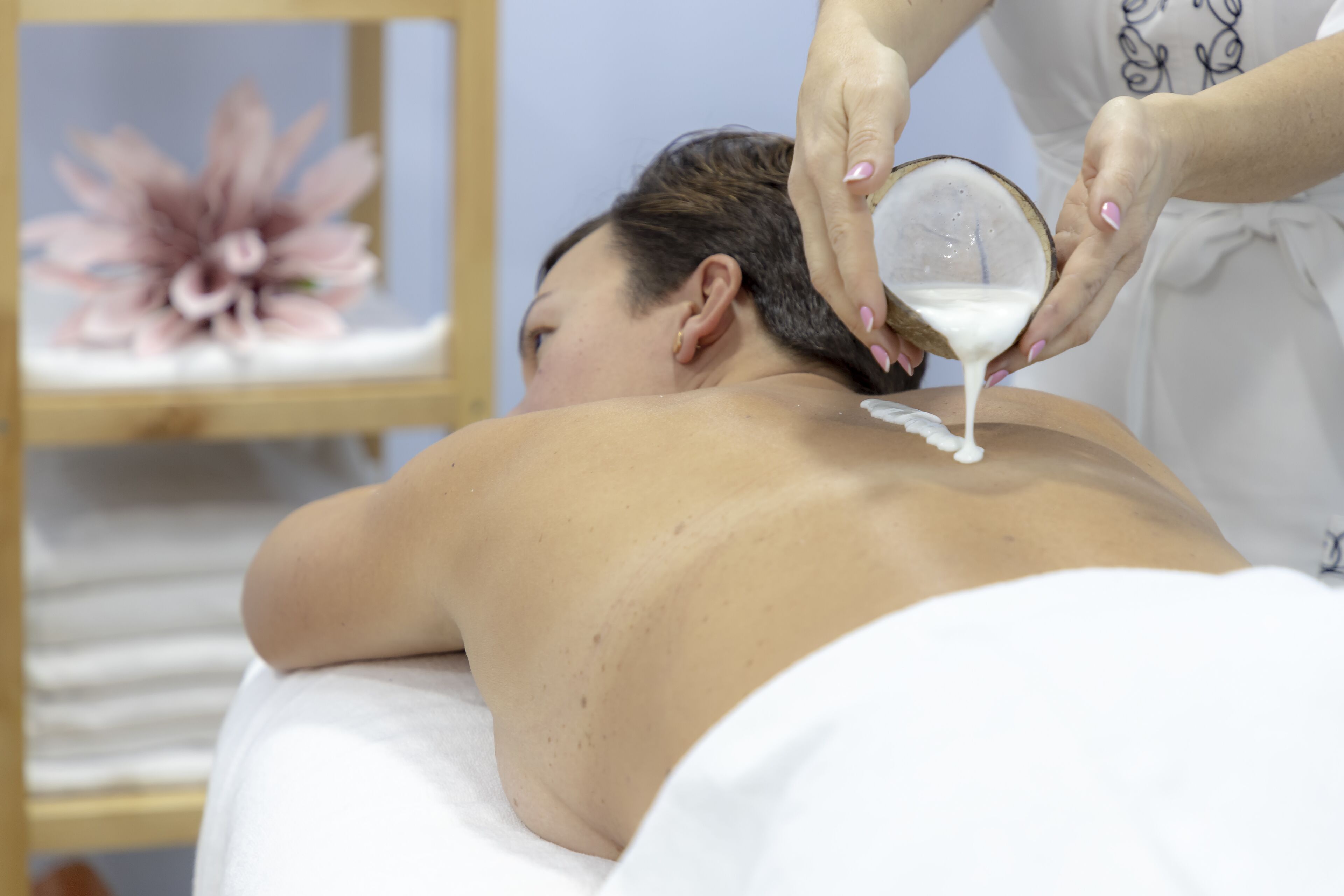 A person receiving a massage with a white towel and a flower in the background.