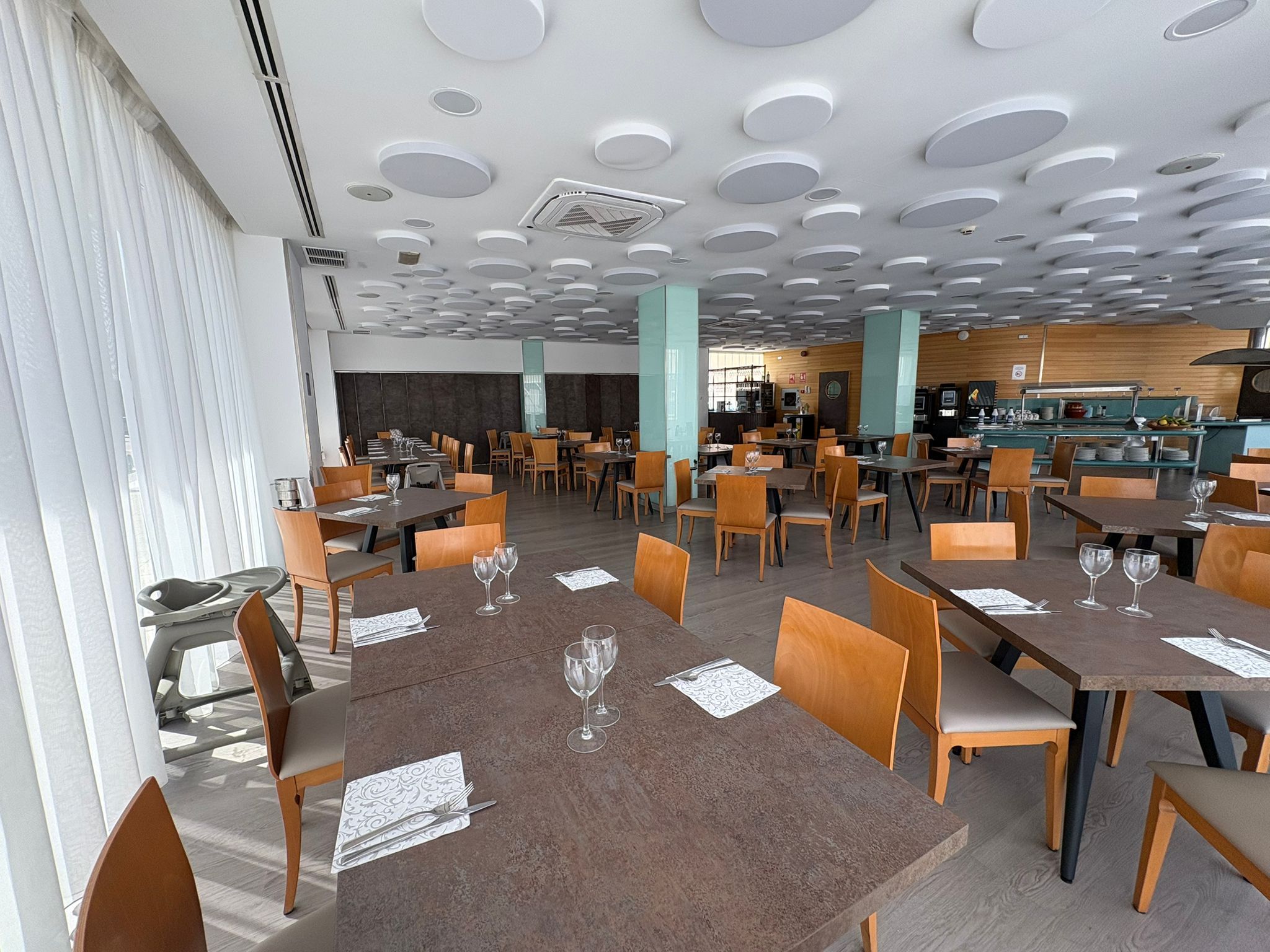 A spacious restaurant with multiple dining tables and chairs, a bar area, and a modern ceiling design.