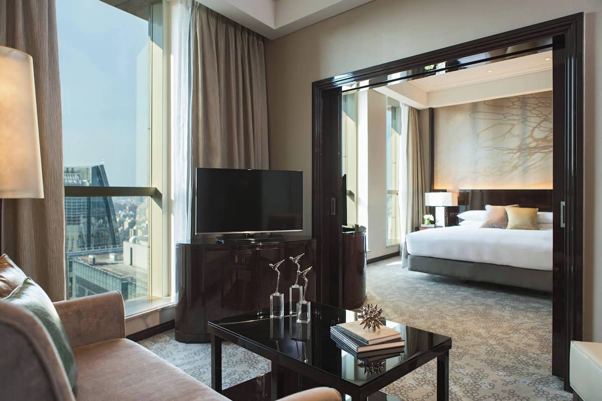 A hotel room with a large bed, a TV, a coffee table with decorative items, and a view of the city.