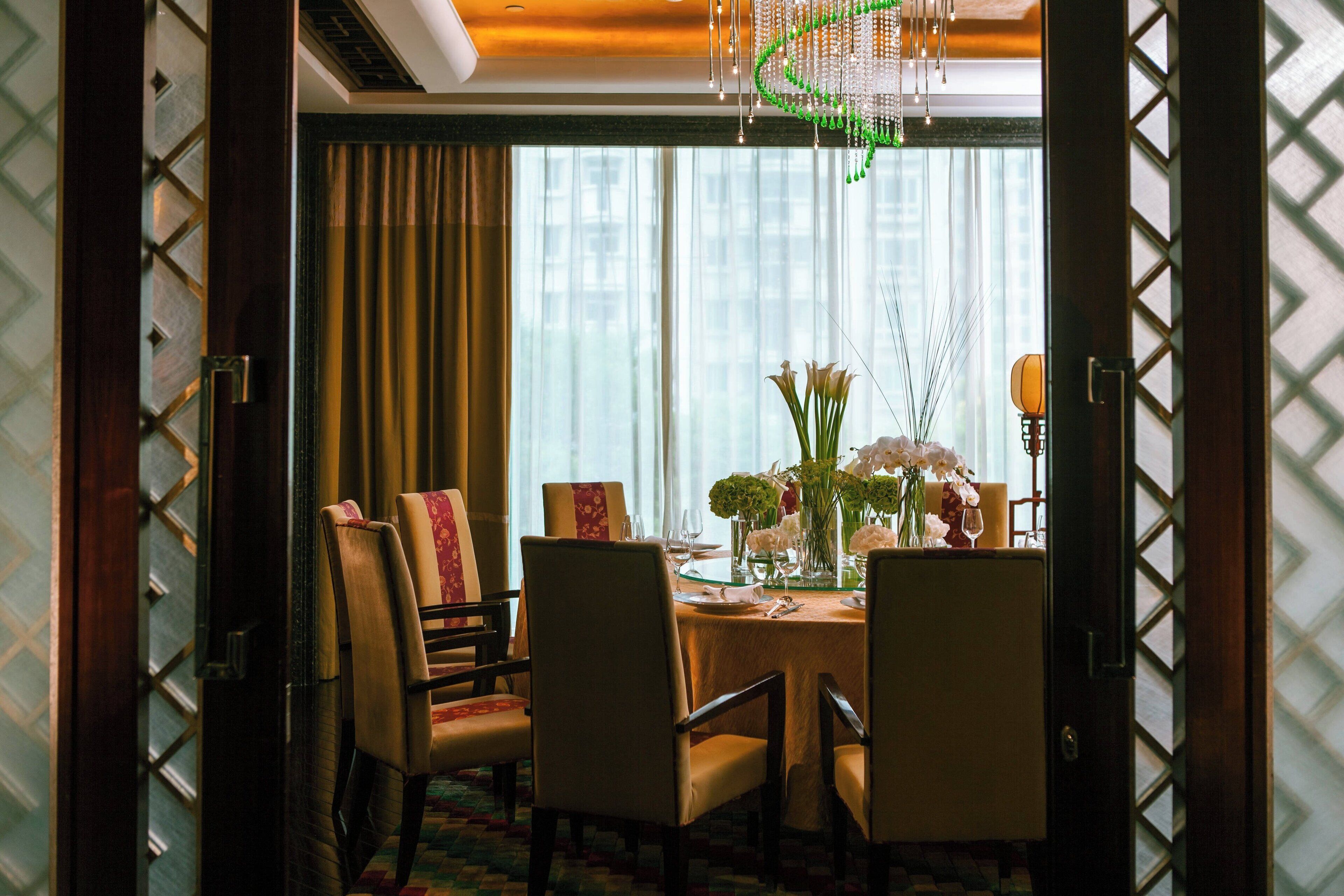 Un comedor con una mesa dispuesta para cuatro personas, rodeado de sillas, y un florero con flores sobre la mesa.