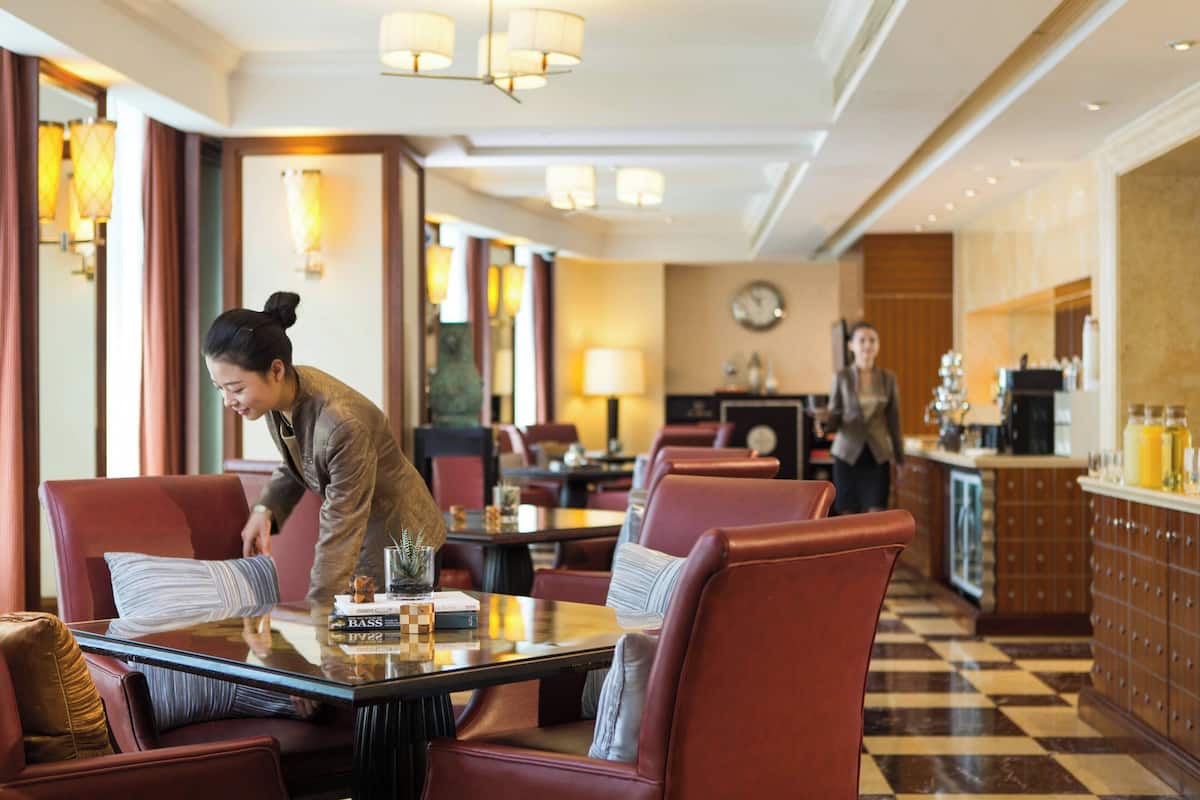 A hotel dining area with red upholstered chairs, a glass-top table, and a bar area with a checkered floor.