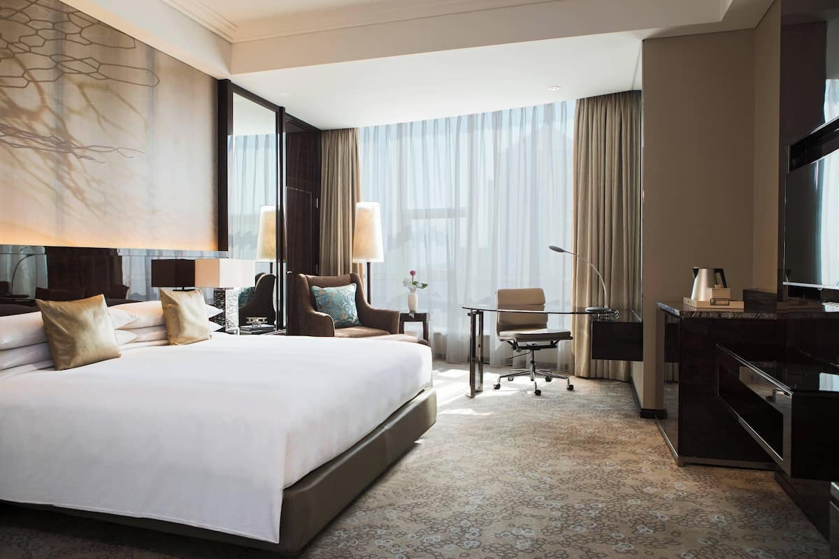 A hotel room with a large bed, a desk, a chair, a TV, and a window with curtains.
