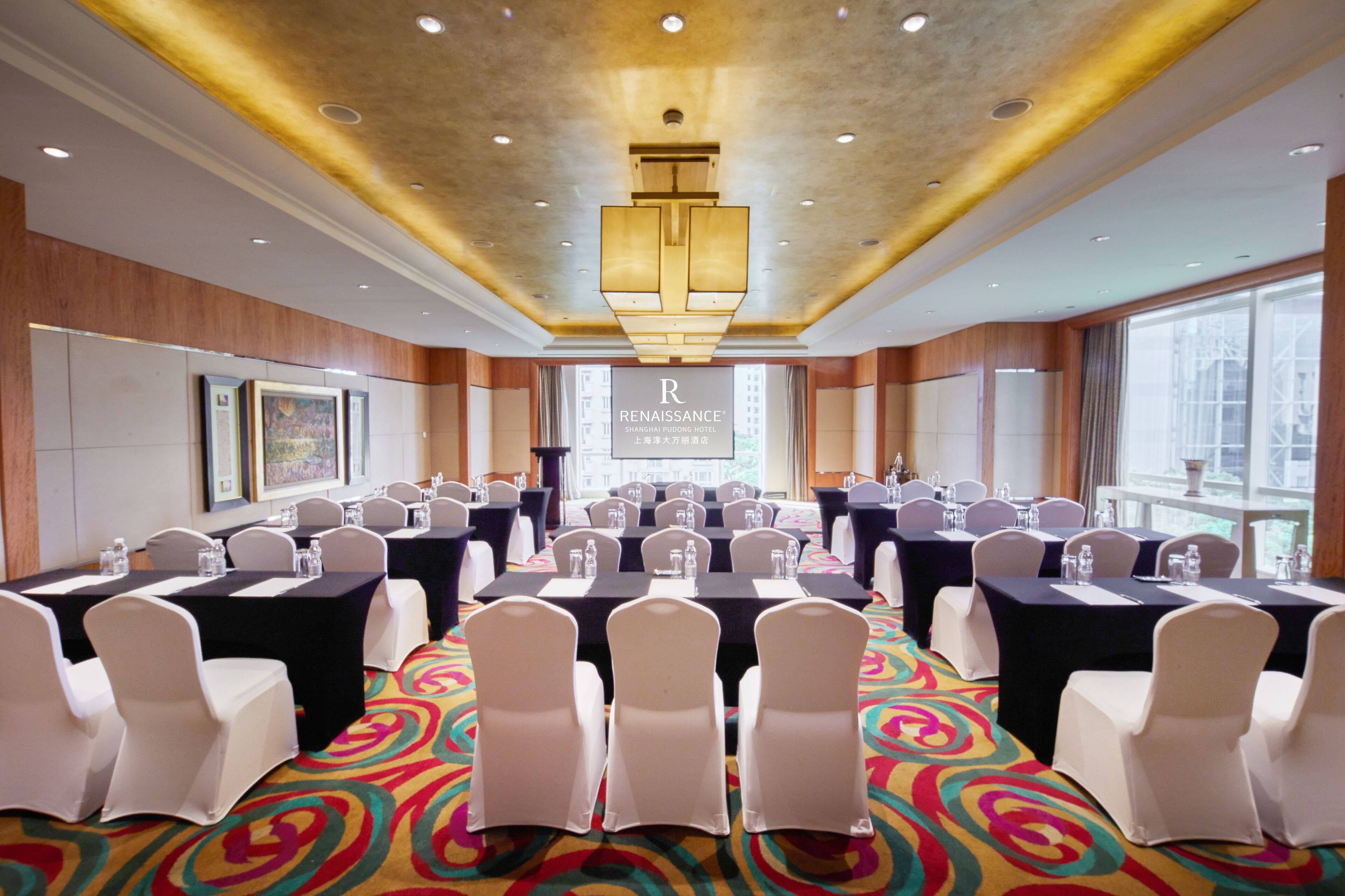 A conference room with multiple tables and chairs, a colorful carpet, and a chandelier.