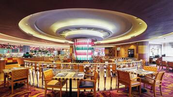 A spacious hotel lobby with a central circular decorative feature, multiple seating areas, and a variety of tables and chairs.