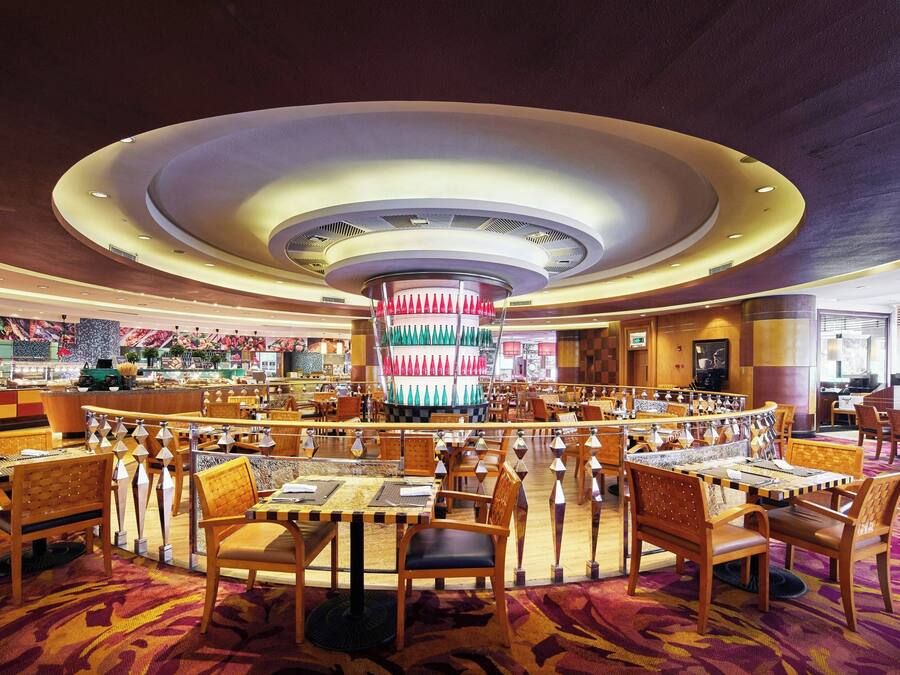 A spacious hotel lobby with a central circular decorative feature, multiple seating areas, and a variety of tables and chairs.