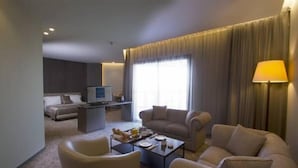 A modern hotel room with a sofa, armchairs, a coffee table, and a TV. - PROMENADE HOTEL ZALKA (Zalqa)